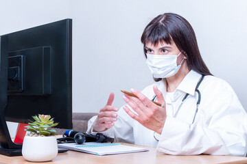 A woman doctor in a medical mask makes an online video call, discusses, gestures. Telemedicine video conferencing remote computer application virtual meeting