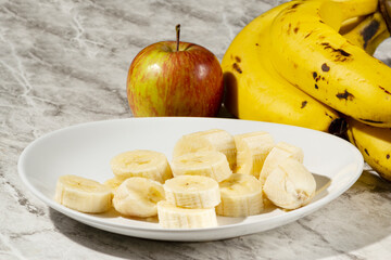 A bunch of bananas, a sliced banana, and an apple on a plate on a table. Selective focus
