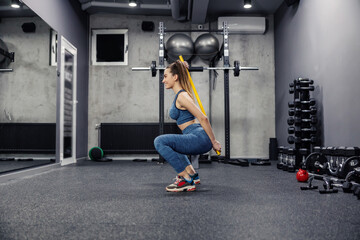 Fototapeta na wymiar Squats with correction bar. Side view of an attractive slender woman in sportswear and in good shape doing squats with a bar for stability. Straighten and proper posture, muscle flexibility and sport