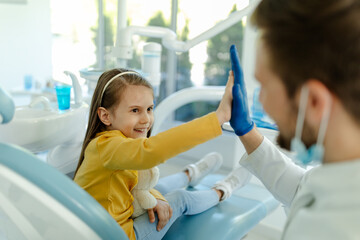 Man doctor is giving hi five to little girl after a successful dental examination.