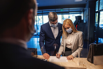 A middle-aged couple with face masks standing at reception and checking in a hotel. Weekend activities, travel destinations, covid pandemic, a business trip during coronavirus