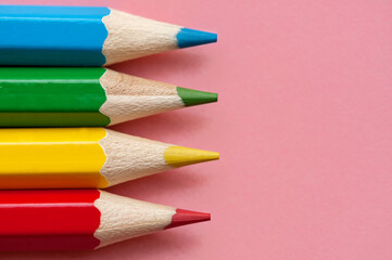 Red, blue, green and yellow pencils on a pink background. Close up