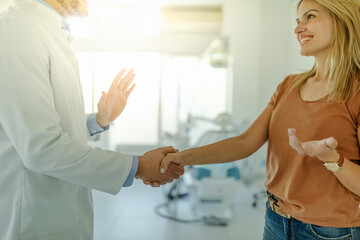 Male dentist and patient are shaking hands in a dental office after a successful dental treatment.