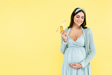 smiling pregnant woman holding ripe banana isolated on yellow.