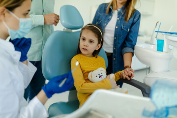 girl looks scared at the dentist before the treatment, while her mother holds her hand for support.
