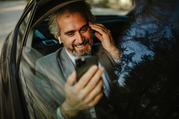 Happy middle aged businessman using cell phone in car, having video call.