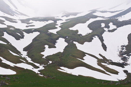 Small scattered patches of snow form a pattern over a green hill, Pena Ubina, Ubinas-La Mesa Natural Park, Asturias, Spain.