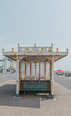 Antiguo banco de madera de color verde botella, parte de una caseta de hierro blanco oxidado envejecido y ventanas de cristal, junto al paseo de la costa de Brighton, Reino Unido