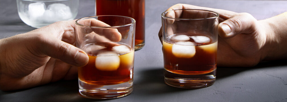 Alcohol. Bottle of whisky. Hands holding glasses of scoth with ice. Male female Acoholism.Banner