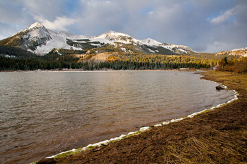 Early morning light scatters across snow-covered peaks above Lost Lake in the Raggeds Wilderness in Colorado. Autumn in the mountains of Colorado bring a swath of colors and light snow before deep winter snows.
