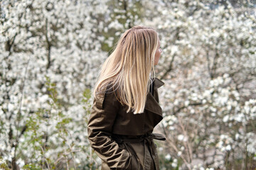 Beautiful young girl walks among the flowering trees of Magnolia in the park. Happy woman enjoys flowers flavors and spring mood. White blooming trees. Spring season concept. Walk outdoors