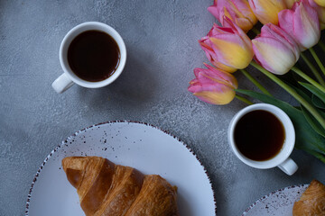 Coffee with croissant and pink tulips on gray background
