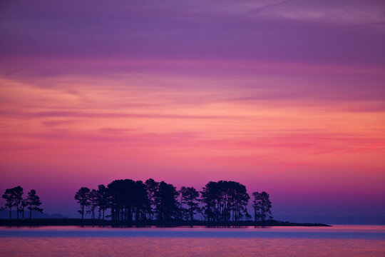 Scenic of trees and water at dawn on a peninsula against a the pink and purple sky just before sunrise in Chesapeake Bay, Tighlman Island, MD.