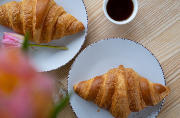 Coffee with croissant and pink tulips on wood background	