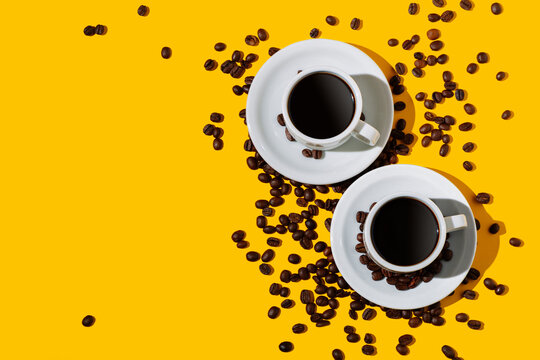 Top view of two coffee cup over a bright yellow color background and many beans spilled around. Flat lay photo with copy space. © AlexPhotoStock