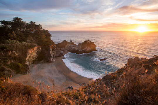The sun sets in a spectacular fashion as the McWay Falls drop eighty feet down to the sand along California's dramatic Big Sur coast.