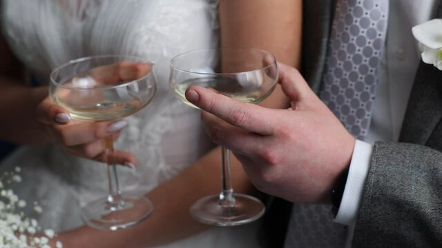 Two wide glasses with white sparkling wine in the hands of the bride and groom. Sparkling champagne in the hands of the couple.