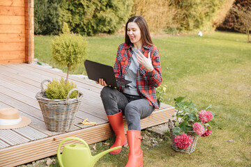 Gardener with laptop in the garden explains something online and is very happy. Woman on vacation...