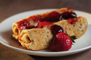 Pancakes or crepes rolls poured strawberry jam and decorated fresh strawberries.