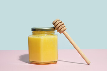 Honey glass jar and honey dipper on minimal coloured background.