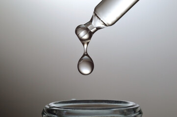 A drop falls from a pipette into a cosmetic bottle on a gray gradient background. close-up.