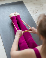 Resistance band exercise at home. Woman doing pilates workout using elastic strap pulling with arms for shoulder training on yoga mat indoors. Sport and healthy active lifestyle concept.