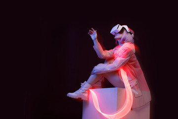 Beautiful woman with purple hair in futuristic costume over dark background. Girl in glasses of virtual reality. Augmented reality game, future technology, AI concept. VR. Red neon light.