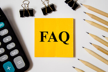 FAQ the word is written on a yellow piece of paper on a white background near a calculator and a pen