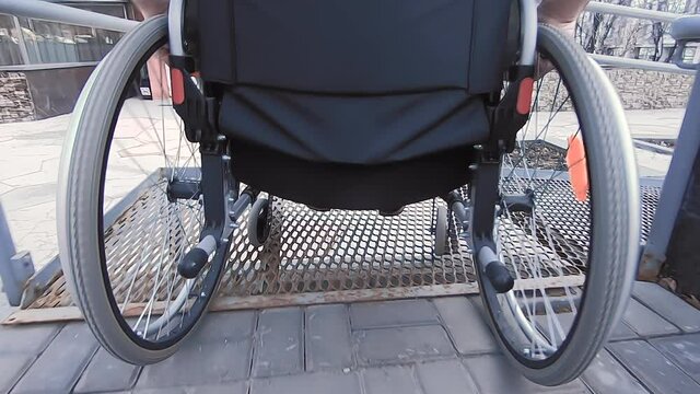 A man with disabilities moves along the street in a wheelchair, goes down the ramp. 