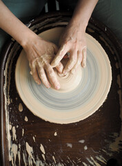 Young female master working on a potter’s wheel, creates clay dishes, view from above