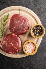 The raw beef meat steak with salt, pepper and rosemary on cutting board.