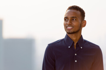 Happy African businessman outdoors at rooftop smiling and thinking