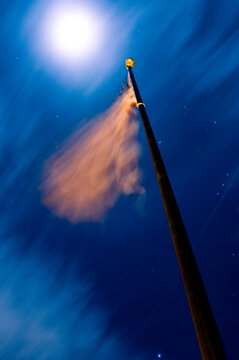 The moon lit flag waves at the Ventura Pier while a jet flies over head underlining Orion's Belt in Ventura, California.