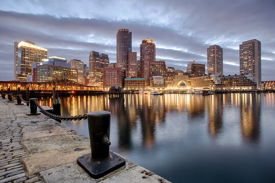 The lights of downtown reflect on the waters of the Fort Point Channel at sunset in Boston, MA.