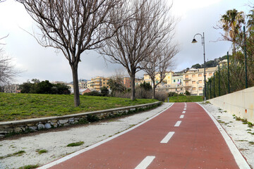 Bike path without people in a green area in Genoa city. In the background the buildings of Pra district.