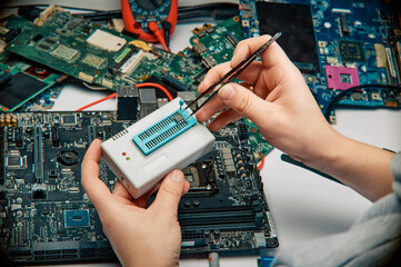 An engineer in a workshop encodes the firmware against the background of the motherboard.