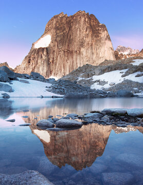 Vertical landscape of the granite feature, Snowpatch Spire, in Bugaboos Provincial Park, British Columbia, Canada as seen at sunrise reflecting in an alpine glacial lake.
