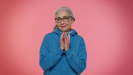 Sneaky cunning mature granny woman with tricky face gesticulating and scheming evil plan, thinking over devious villain idea, cunning cheats, jokes and pranks. Senior grandmother on pink background