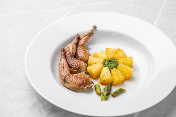 Modern restaurant dish of roasted quail legs decorated with pineapple slices. pesto and asparagus