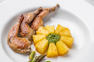 Modern restaurant dish of roasted quail legs decorated with pineapple slices. pesto and asparagus
