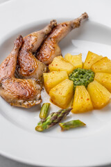 Modern restaurant dish of roasted quail legs decorated with pineapple slices. pesto and asparagus