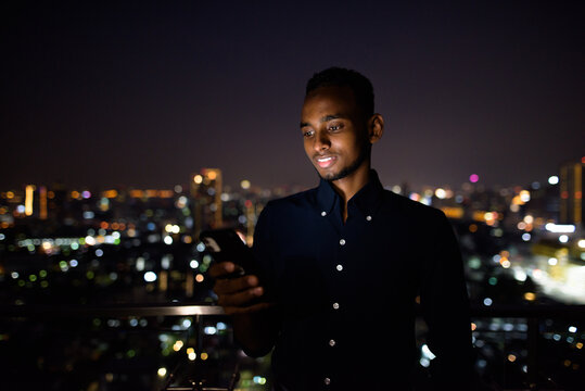 Happy African businessman outdoors at rooftop using phone at night