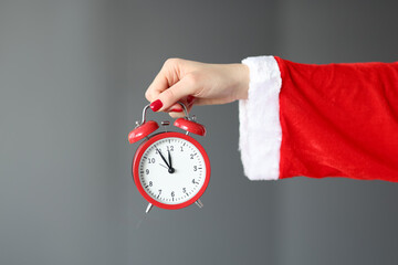 Hand in santa claus costume holds red alarm clock.