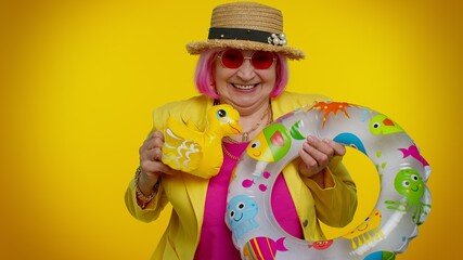 Traveler tourist senior stylish granny woman play with swimming ring and inflatable duck toy, ready for travel on weekends. Summer vacation, journey trip to seaside. Elderly grandmother on orange wall
