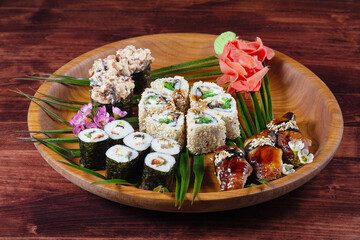 Sushi and rolls on wooden plate with spices and green leaves