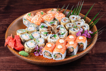 Sushi or rolls with ginger and spices on wooden plate with green leaves