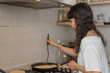 Latin woman dressed casually in the kitchen stirring eggs with cheese and heating Colombian arepas