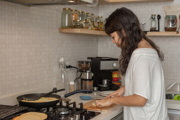 Latin woman dressed casually in the kitchen cutting Colombian arepas while cooking eggs and cheese
