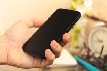 Man hold black smartphone on home interior background, concept of using a mobile phone