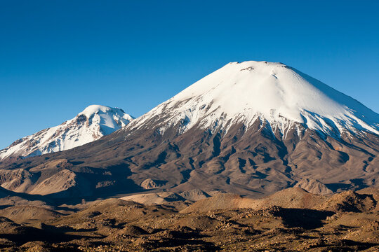 The twin volcanoes of Pomerape (L) in Bolivia's Sajama Nat Park and Parinacota (R) in Lauca Nat Park in northern Chile at sunset.